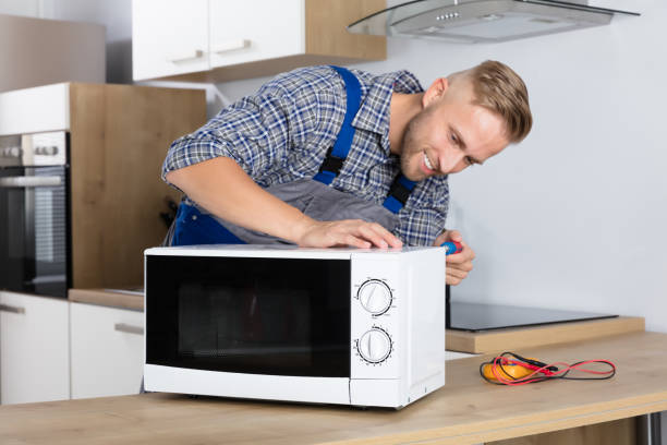 happy male serviceman using screwdriver to repair microwave in kitchen at home